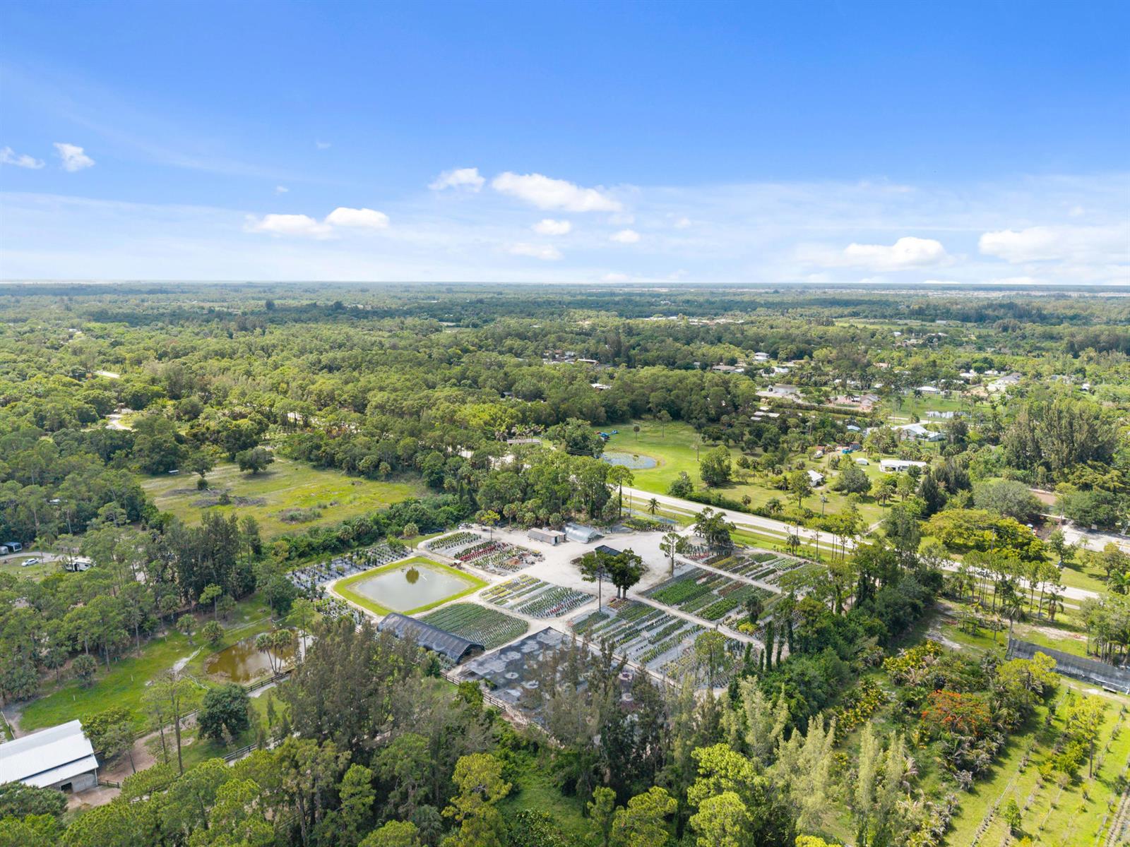 An aerial view shows a plant nursery with greenhouses, rows of plants, and small ponds — 14650 Okeechobee Boulevard, FL 33470, FL