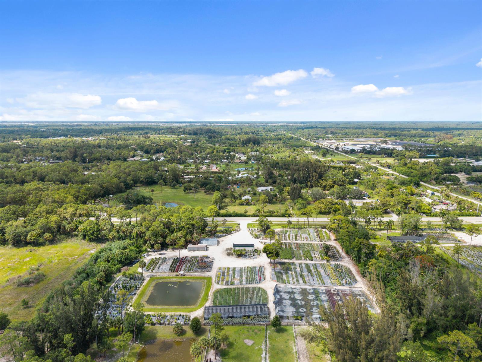 An aerial view shows a plant nursery with rows of crops, greenhouses, and a pond — 14650 Okeechobee Boulevard, FL 33470, FL