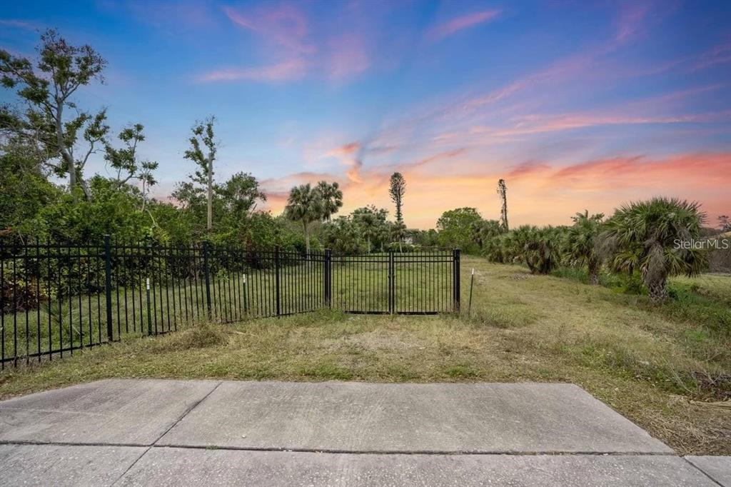 A black metal fence and gate enclose a grassy, undeveloped lot under a sunset sky — ENGLEWOOD ROAD, VENICE, FL
