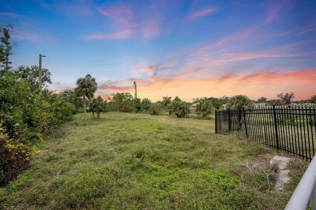 A grassy, undeveloped lot features scattered palm trees under a colorful sunset sky — ENGLEWOOD ROAD, VENICE, FL