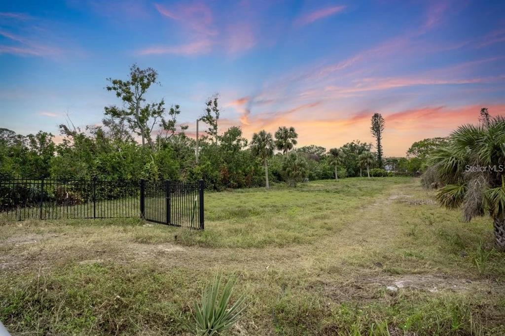 An empty, grassy lot features a black metal fence and scattered trees under a sunset — ENGLEWOOD ROAD, VENICE, FL