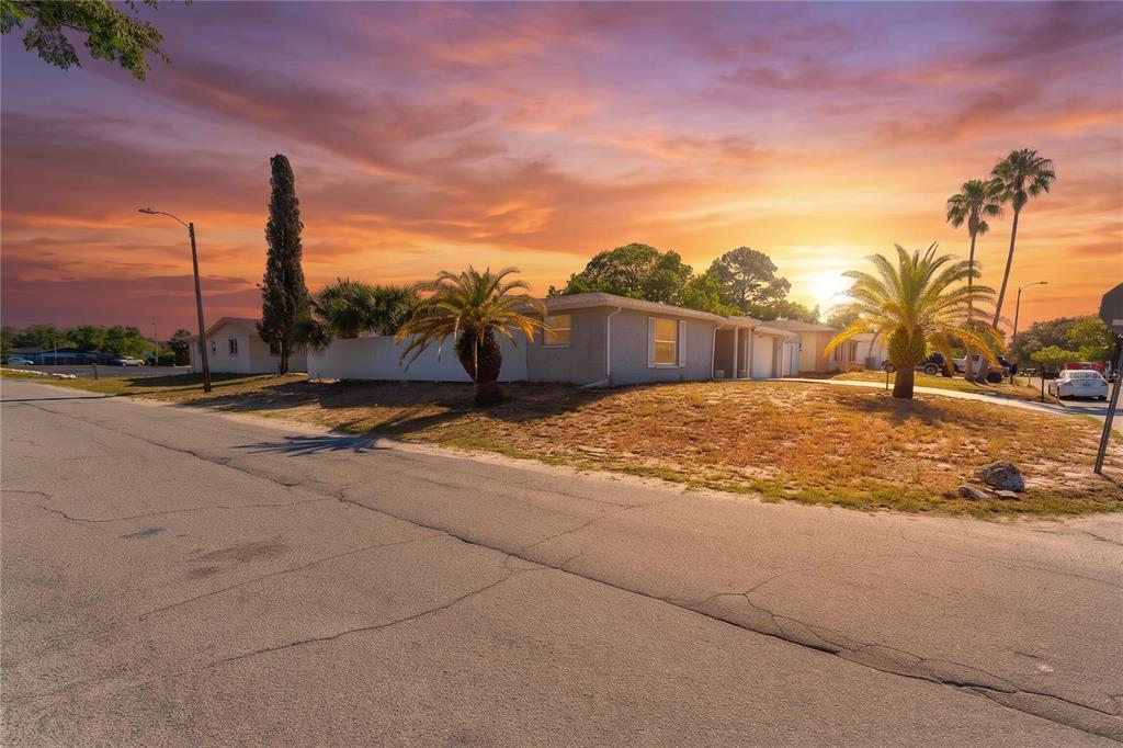 A single-story house with a light-colored exterior sits on a corner lot at sunset — 7511 TYSON DRIVE, PORT RICHEY, FL