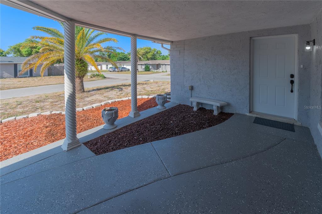 A covered porch features a concrete floor, two decorative columns, and a white front door — 7511 TYSON DRIVE, PORT RICHEY, FL