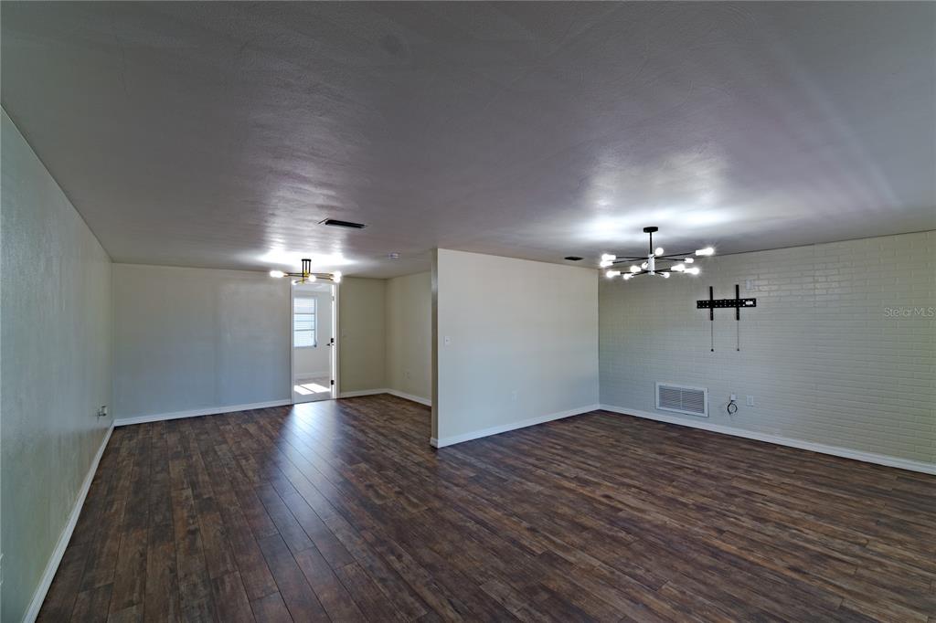 An open living area features dark wood-look flooring, light-colored walls, and two modern light fixtures — 7511 TYSON DRIVE, PORT RICHEY, FL