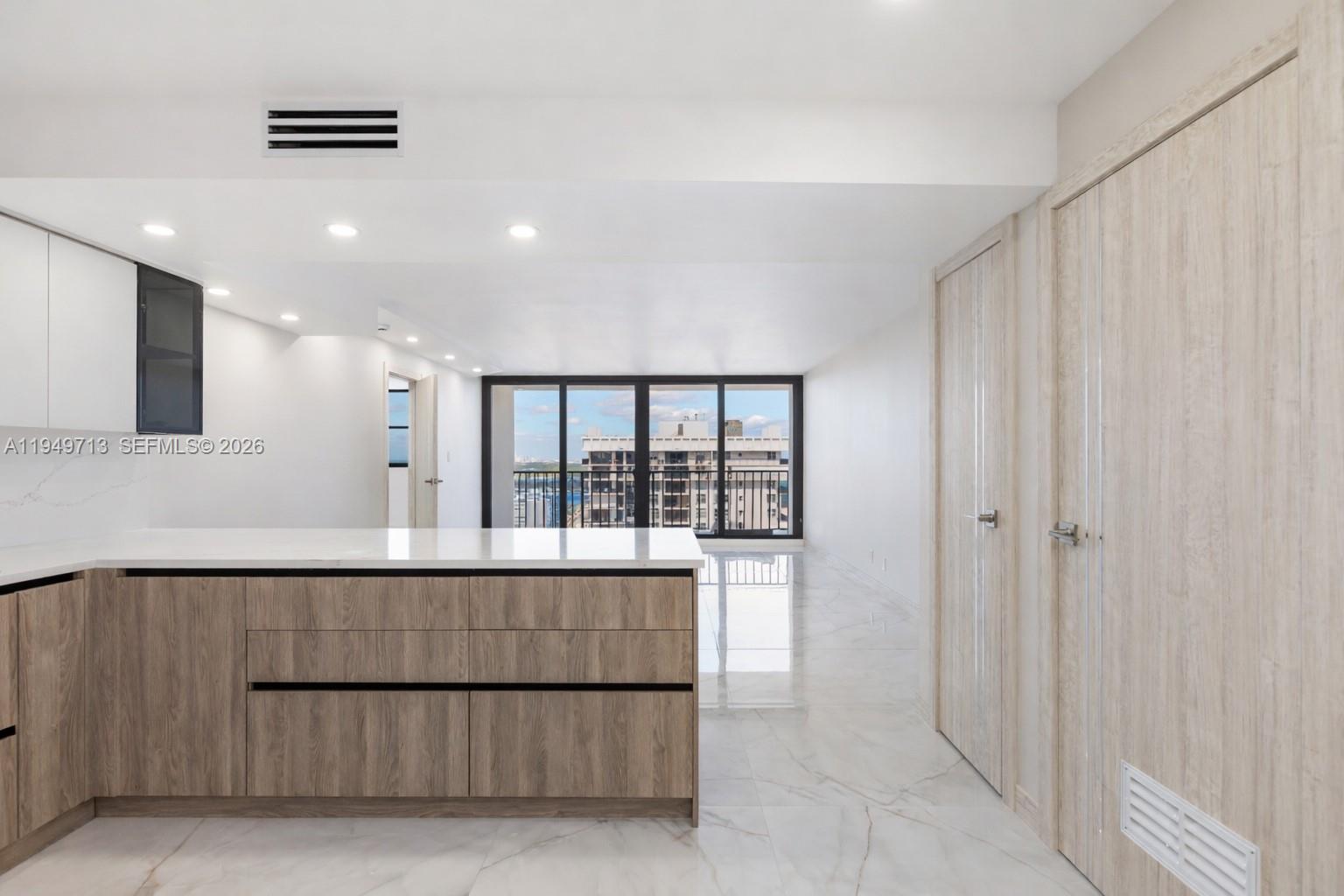 A modern kitchen with wood-grain cabinets and white countertops overlooks a bright living area — 2401 S Ocean Dr # A4, Hollywood FL 33019, HOLLYWOOD, FL
