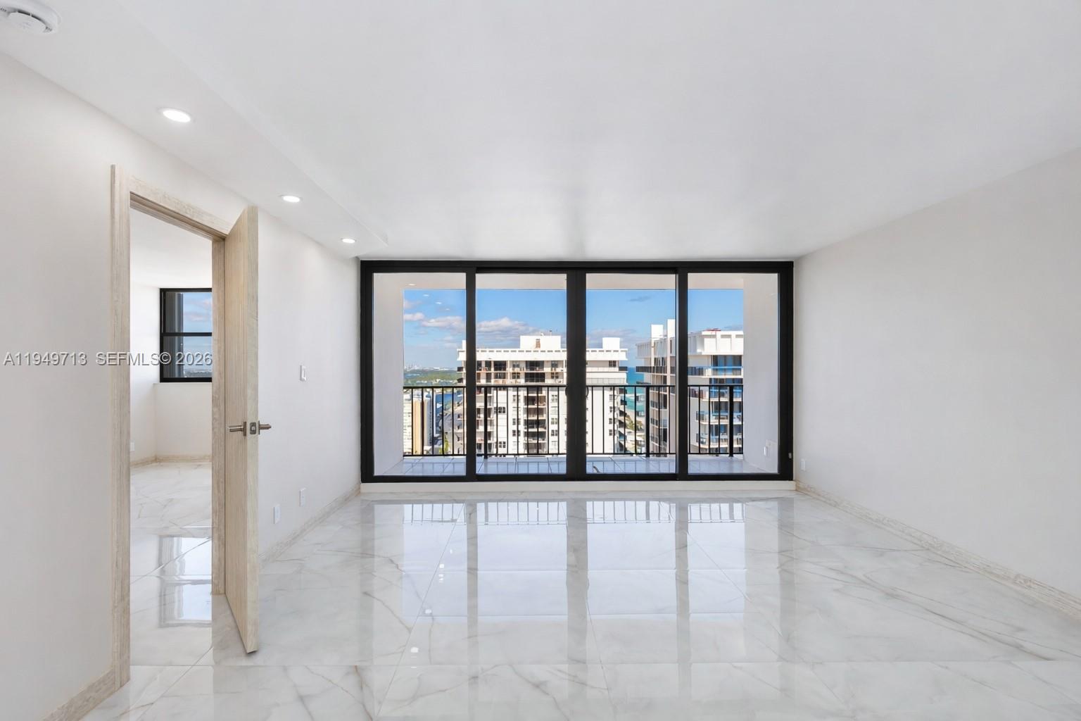 An empty room with white marble floors, recessed lighting, and a balcony overlooking city buildings — 2401 S Ocean Dr # A4, Hollywood FL 33019, HOLLYWOOD, FL