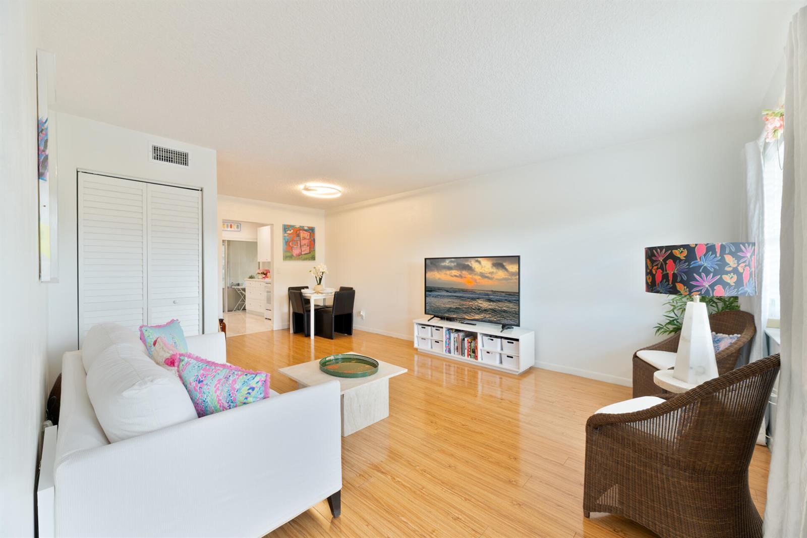 A living room with light wood floors, a white sofa, a television, and wicker chairs — 32 Abbey Lane # 205, Delray Beach FL 33446, DELRAY BEACH, FL