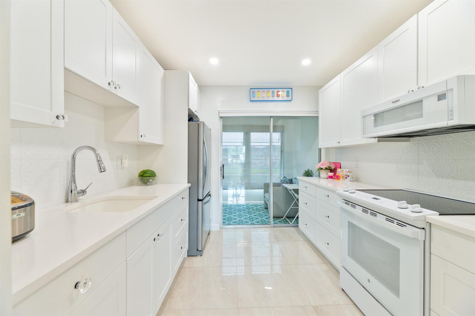 A bright, galley-style kitchen features white cabinetry, quartz countertops, stainless steel appliances, and tile flooring — 32 Abbey Lane # 205, Delray Beach FL 33446, DELRAY BEACH, FL