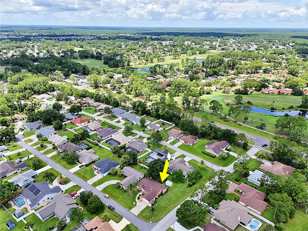 An aerial view shows a suburban neighborhood with houses, green lawns, and a golf course — 2 WINDERMERE PLACE, PALM COAST, FL