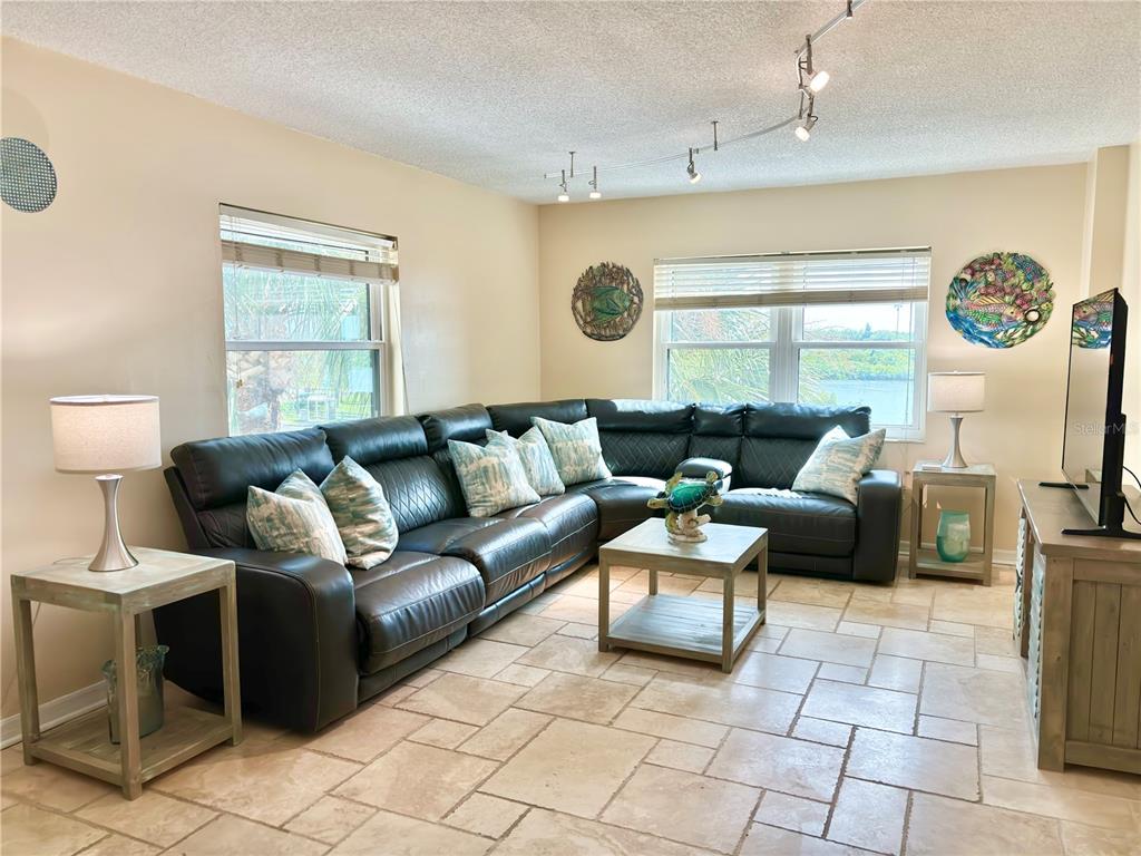 A living room features a large dark leather sectional, tile flooring, and two windows — 18650 GULF BOULEVARD UNIT 315, INDIAN SHORES, FL