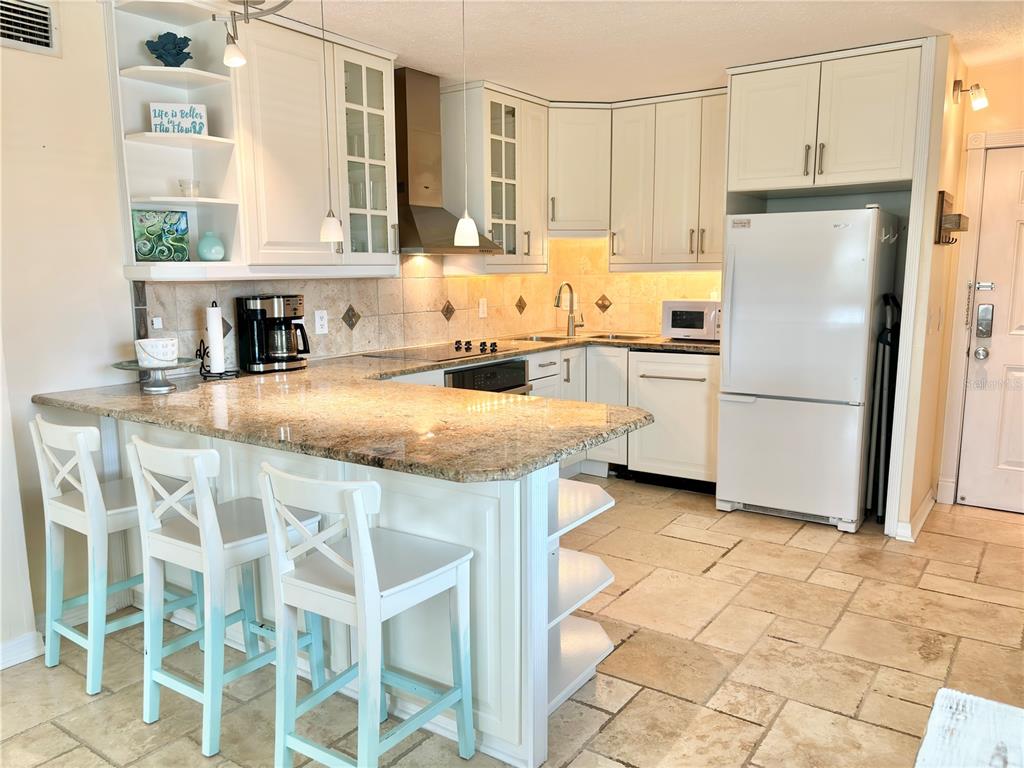 A kitchen features white cabinets, granite countertops, a breakfast bar with stools, and tile flooring — 18650 GULF BOULEVARD UNIT 315, INDIAN SHORES, FL