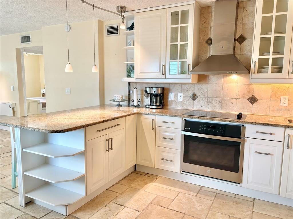 A kitchen features white cabinetry, granite countertops, stainless steel appliances, and light-colored stone flooring — 18650 GULF BOULEVARD UNIT 315, INDIAN SHORES, FL