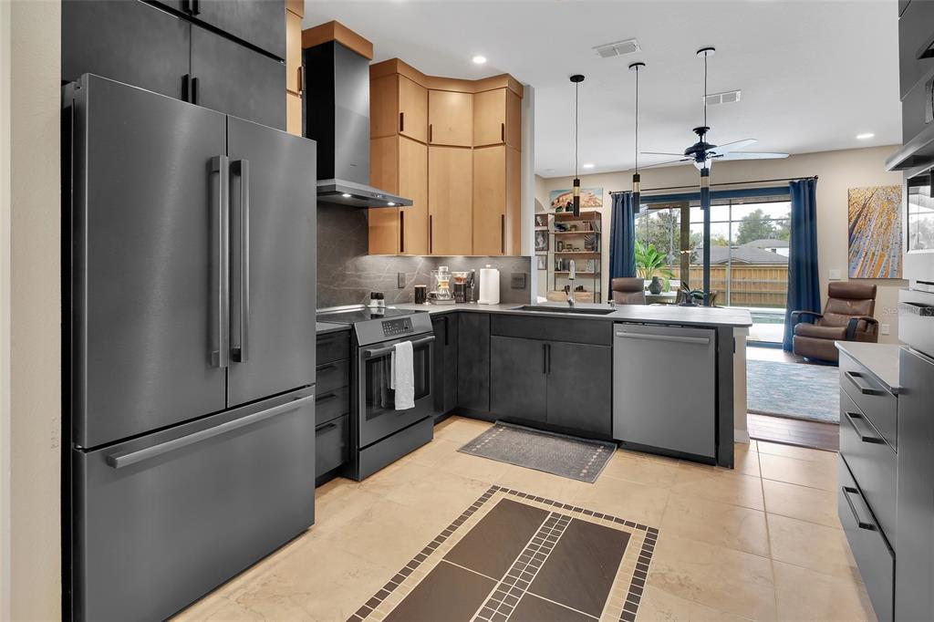 A modern kitchen features dark gray cabinetry, stainless steel appliances, and light wood upper cabinets — 404 COUNTRY VIEW CIRCLE, DELAND, FL