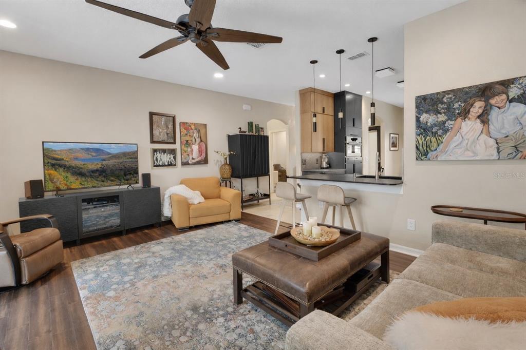 A living room with a television, area rug, leather ottoman, and an open kitchen area — 404 COUNTRY VIEW CIRCLE, DELAND, FL