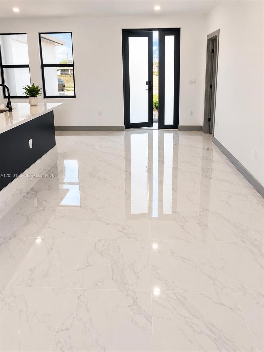 A modern kitchen and living area features white marble-look tile floors and black-framed glass doors — 3000 Nelson Rd N, Cape Coral FL 33993, CAPE CORAL, FL