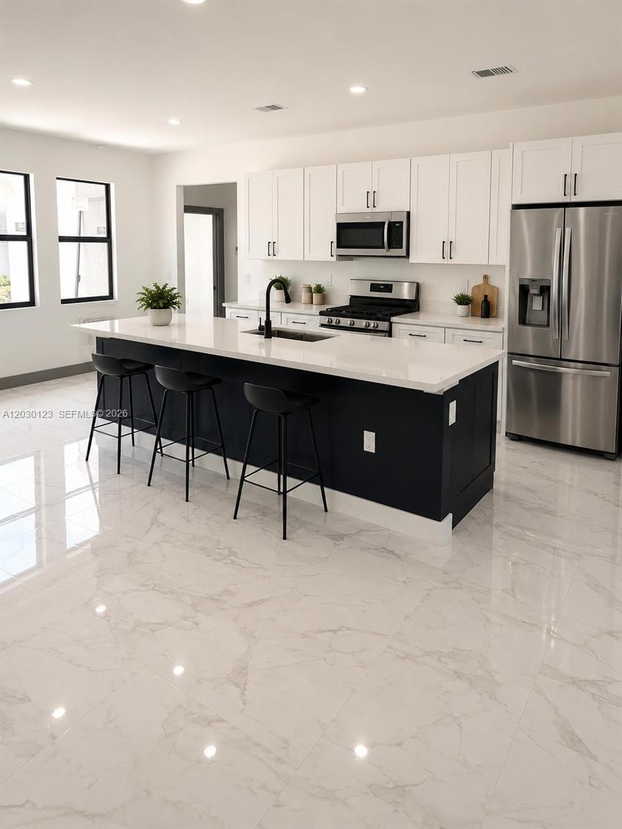 A modern kitchen features a black island with bar stools, white cabinetry, and marble-look flooring — 3000 Nelson Rd N, Cape Coral FL 33993, CAPE CORAL, FL