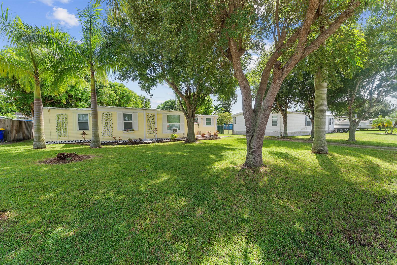 A yellow mobile home sits on a grassy lot shaded by several large trees — 2886 SE La Palma Terrace, Stuart FL 34997, STUART, FL