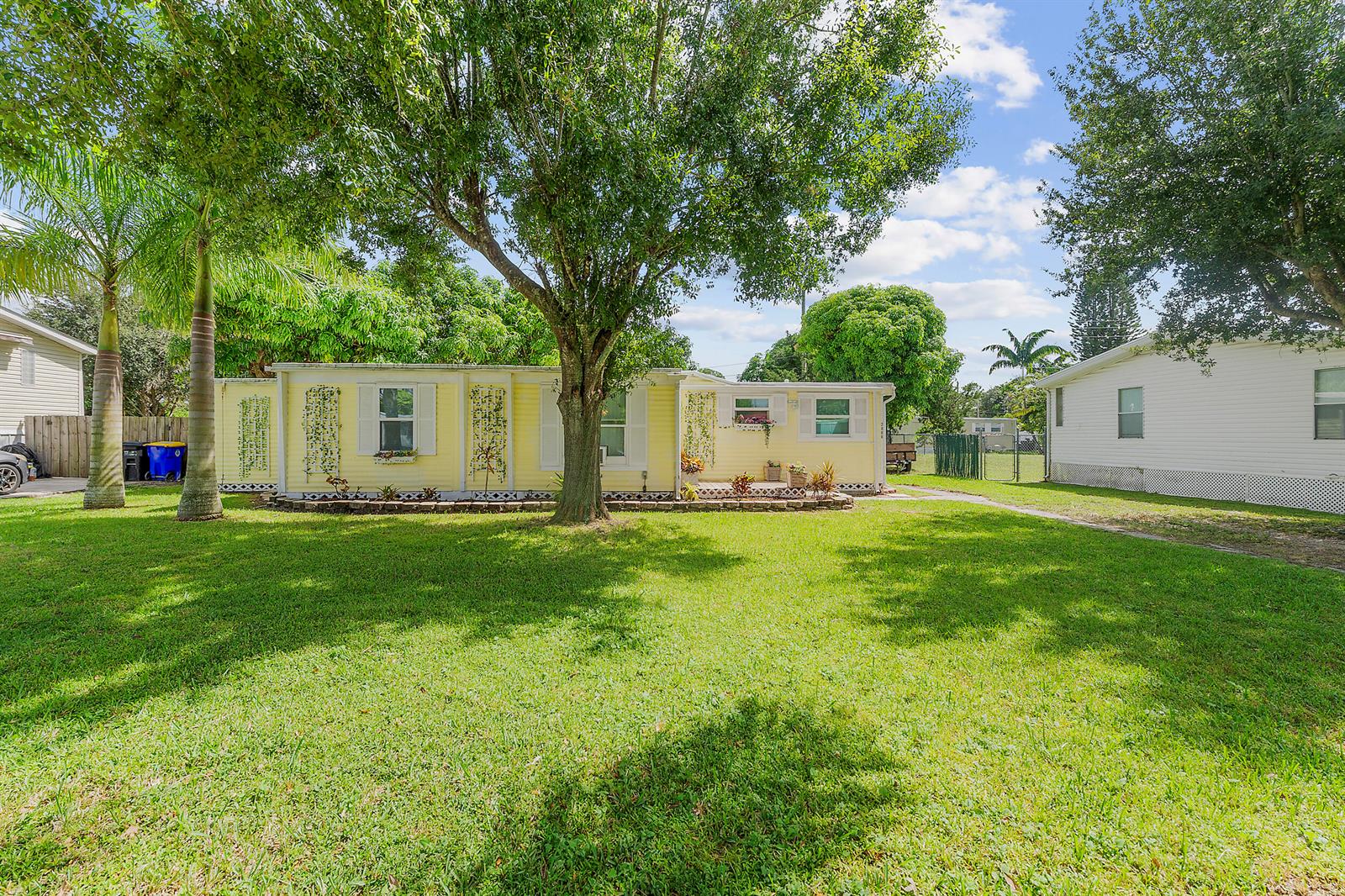 A yellow single-story mobile home sits on a grassy lot with mature trees — 2886 SE La Palma Terrace, Stuart FL 34997, STUART, FL