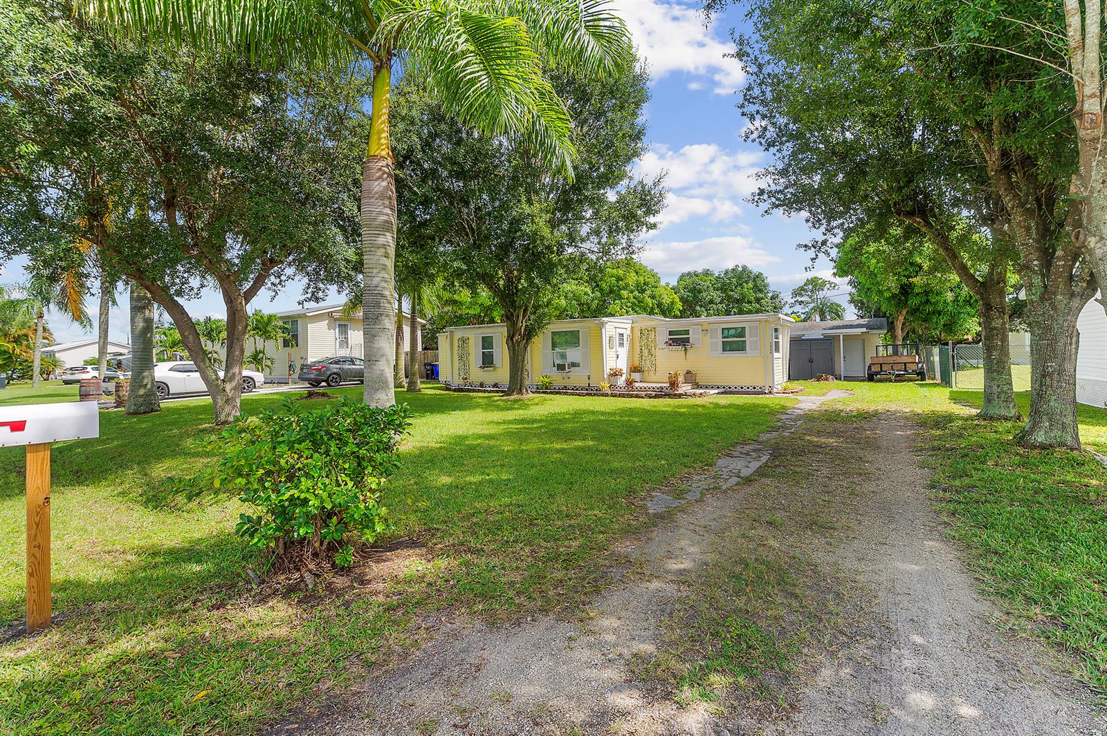A yellow single-story house sits on a grassy lot with a gravel driveway and trees — 2886 SE La Palma Terrace, Stuart FL 34997, STUART, FL