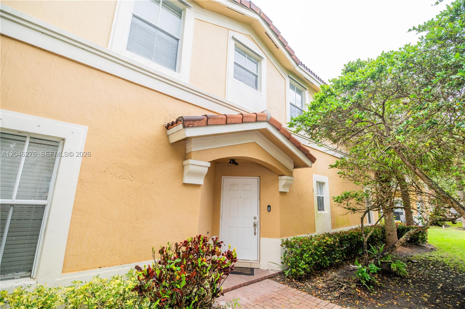 The exterior of a two-story tan stucco home features a covered entryway and landscaping — 3153 SW 129th Ter, Miramar FL 33027, MIRAMAR, FL