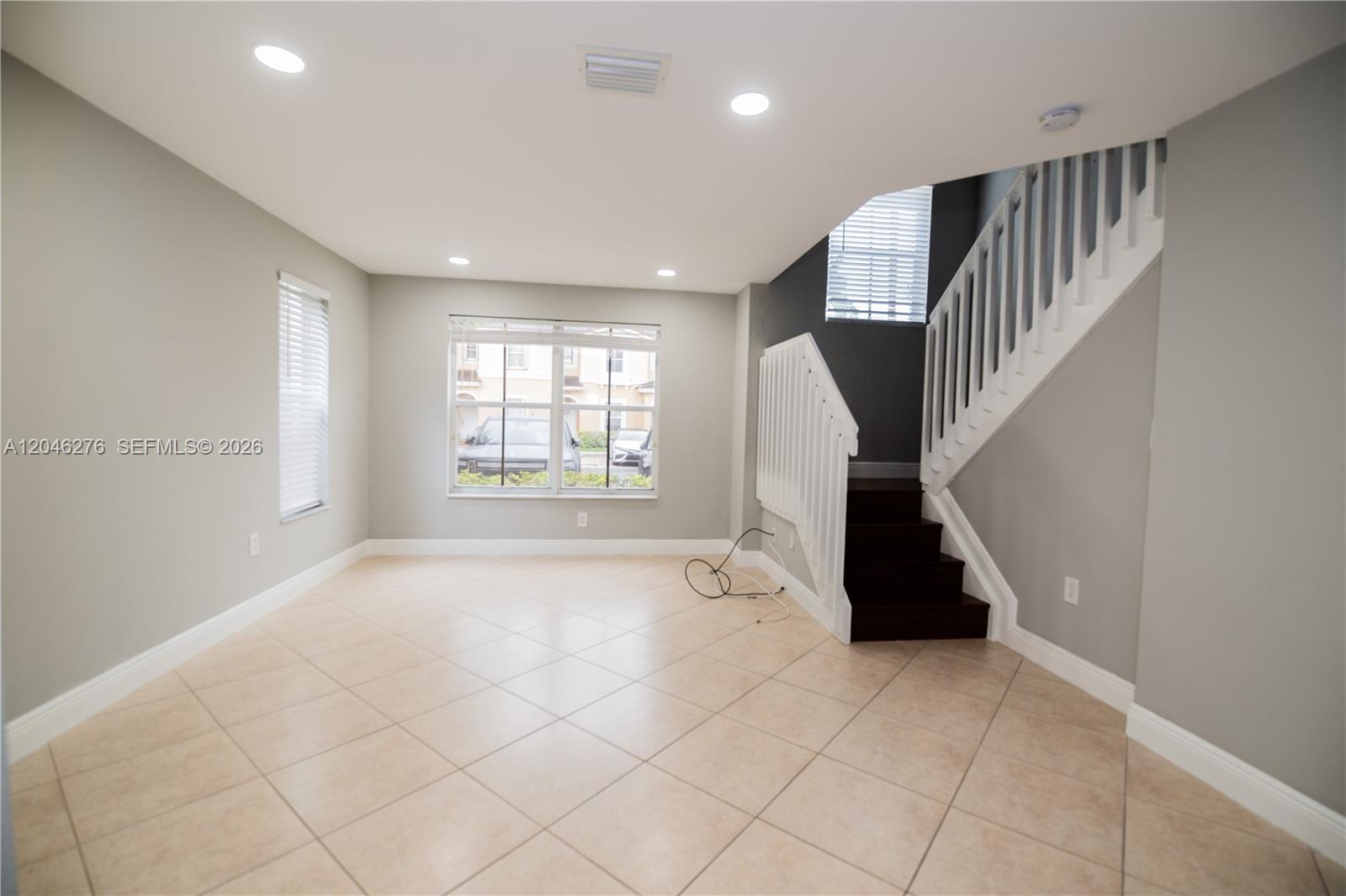 An empty room with tile flooring, gray walls, recessed lighting, and a wooden staircase — 3153 SW 129th Ter, Miramar FL 33027, MIRAMAR, FL