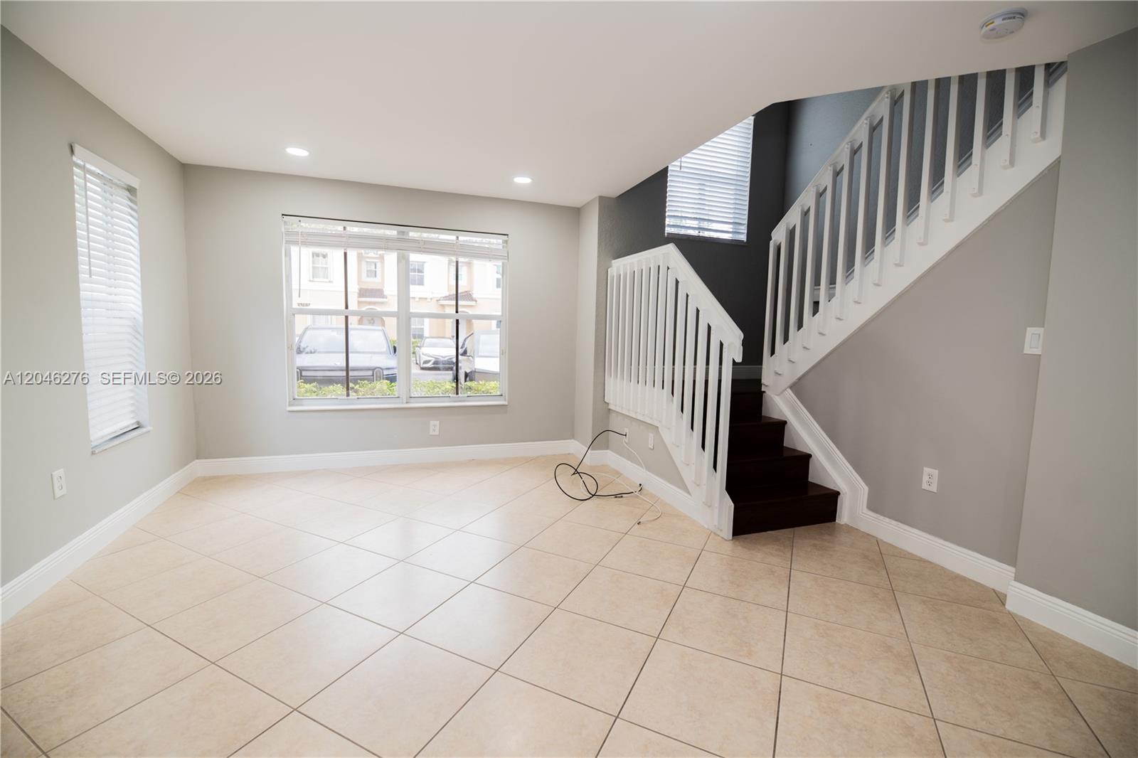 An empty room features light tile floors, gray walls, and a staircase with white railings — 3153 SW 129th Ter, Miramar FL 33027, MIRAMAR, FL