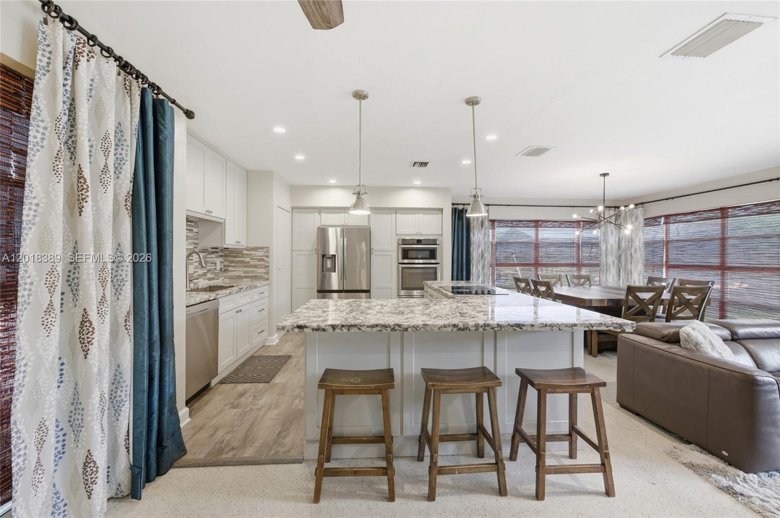 A kitchen features white cabinetry, granite countertops, a central island with bar stools, and appliances — 109 S 57th Ave, Hollywood FL 33023, HOLLYWOOD, FL