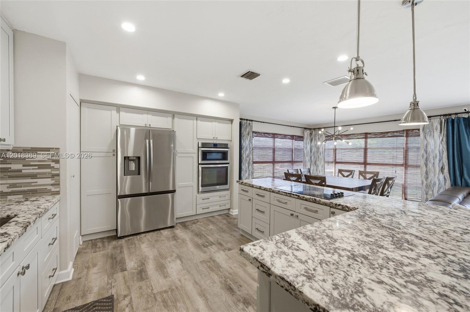 A kitchen features white cabinetry, granite countertops, stainless steel appliances, and wood-look flooring — 109 S 57th Ave, Hollywood FL 33023, HOLLYWOOD, FL