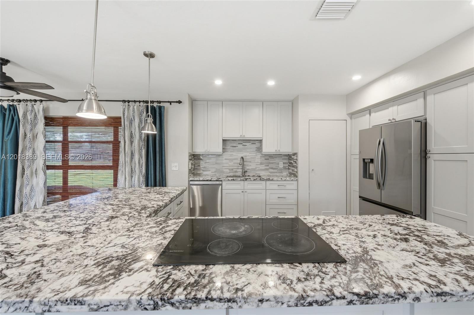 A kitchen features white cabinets, granite countertops, a stainless steel refrigerator, and a cooktop island — 109 S 57th Ave, Hollywood FL 33023, HOLLYWOOD, FL