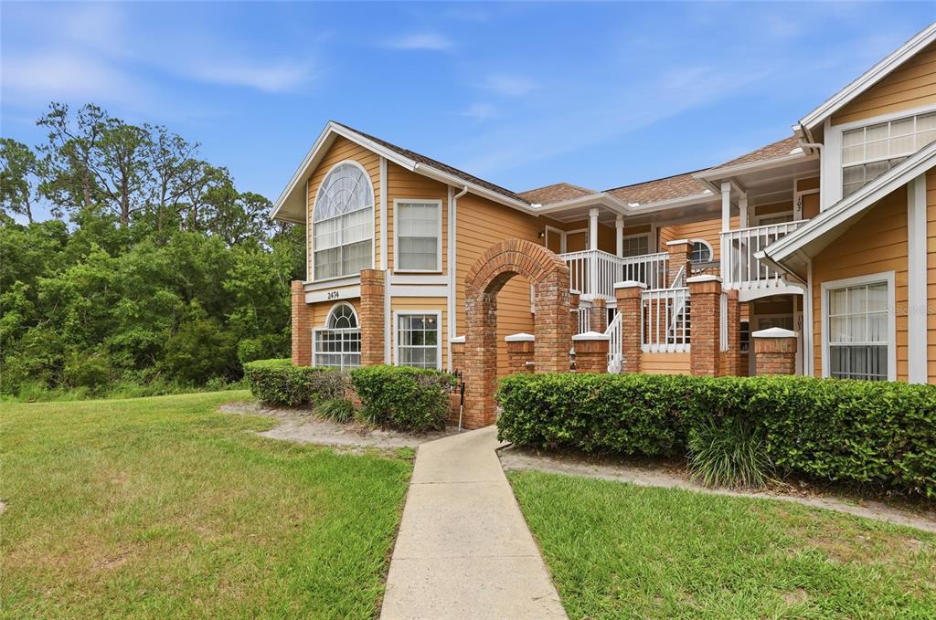 A two-story apartment building with yellow siding, brick accents, and a concrete walkway — 2474 SWEETWATER CLUB CIRCLE UNIT 101, KISSIMMEE, FL