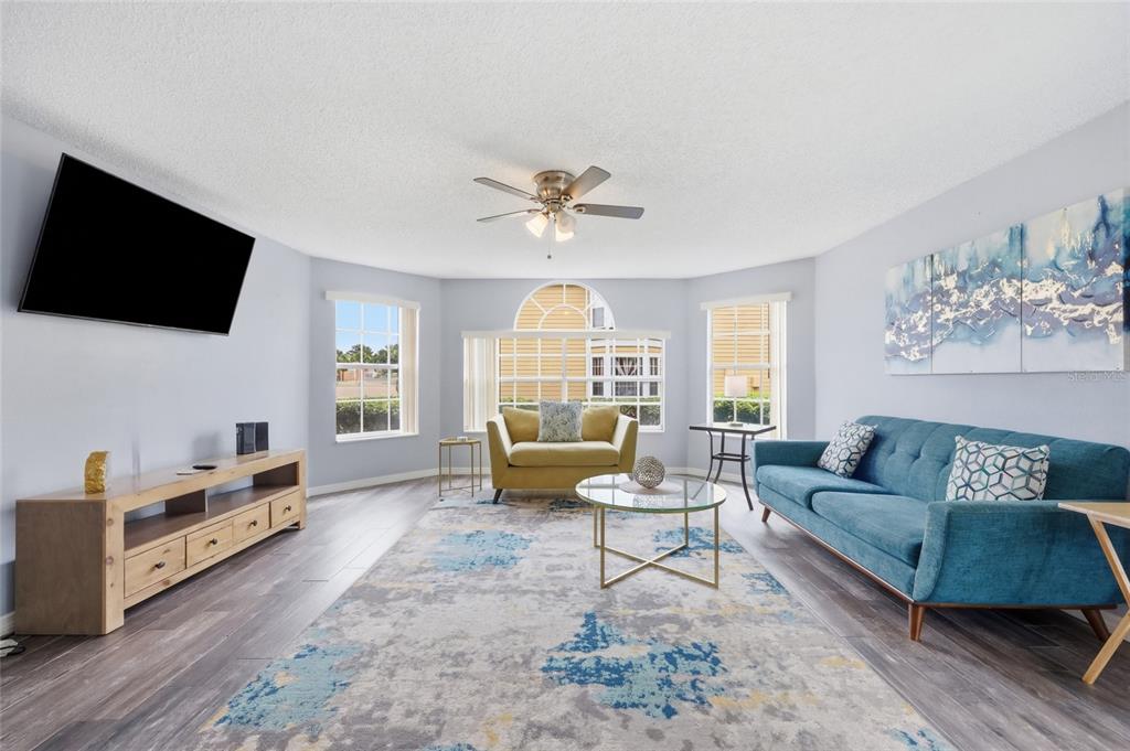A living room features a blue sofa, yellow armchair, area rug, and wood media console — 2474 SWEETWATER CLUB CIRCLE UNIT 101, KISSIMMEE, FL