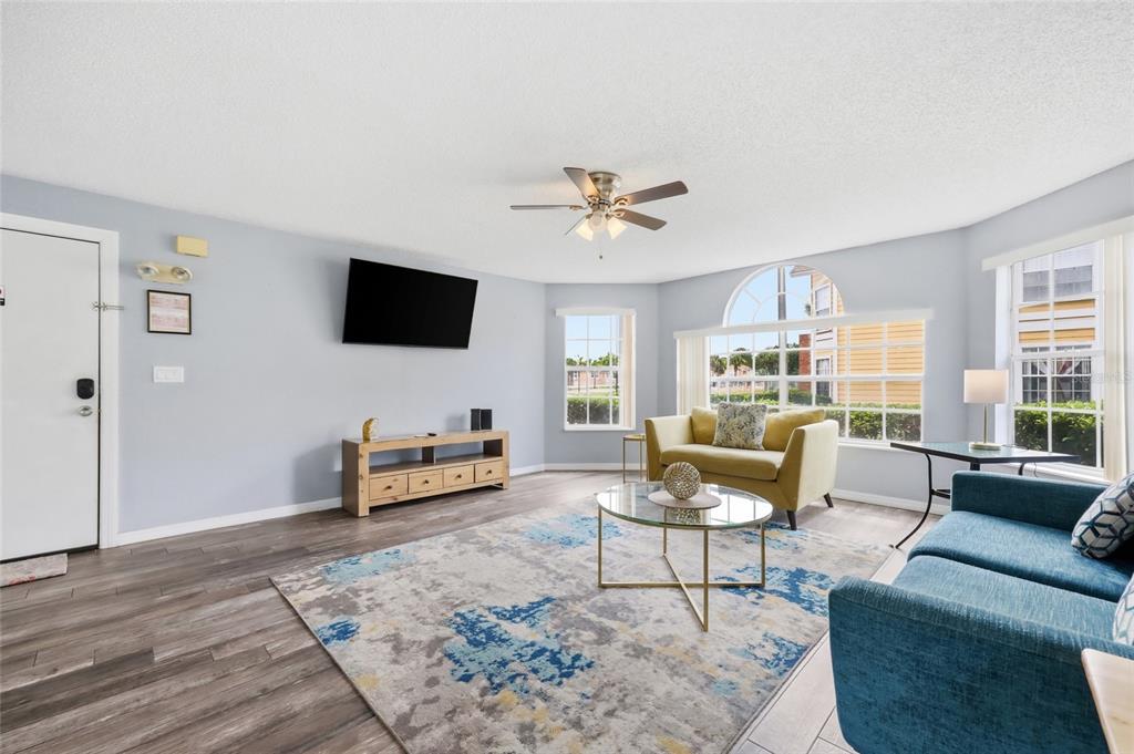 A living room features light blue walls, wood-look flooring, a ceiling fan, and large windows — 2474 SWEETWATER CLUB CIRCLE UNIT 101, KISSIMMEE, FL