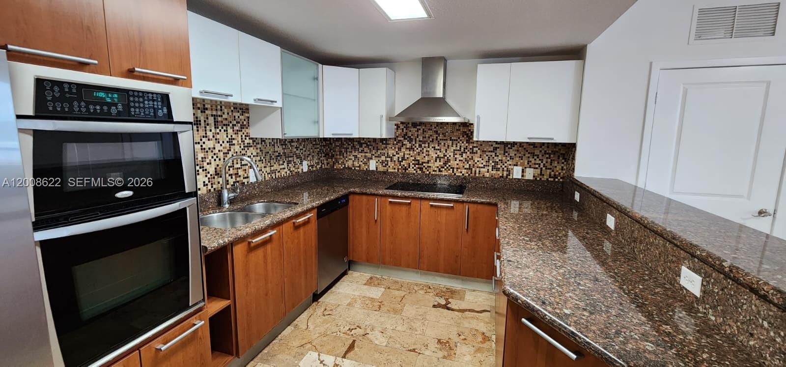 A kitchen features wood cabinets, white upper cabinets, granite countertops, and a mosaic tile backsplash — 170 SE 14th St # 1408, Miami FL 33131, MIAMI, FL
