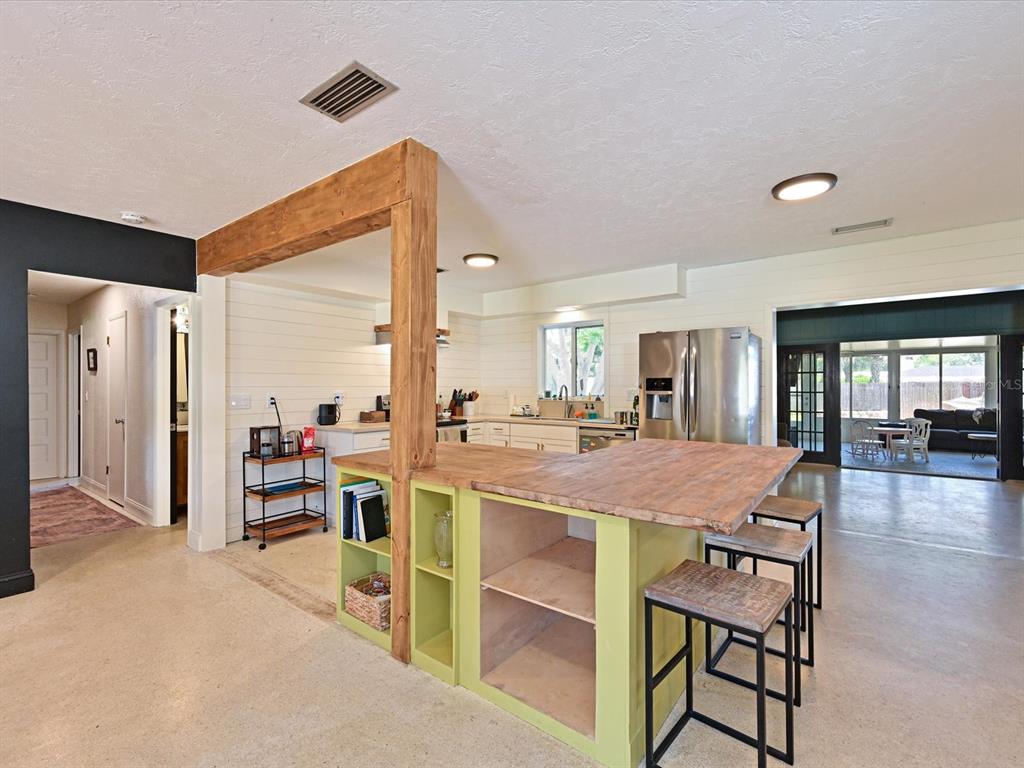 A kitchen features a wooden island with open shelving, bar stools, and a rustic support beam — 5812 2ND AVE DR NW, BRADENTON, FL