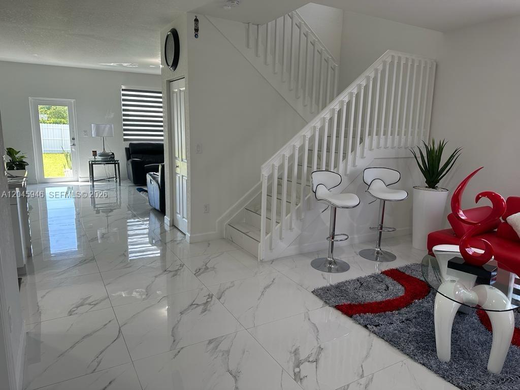 A bright living area features white marble floors, a staircase, and modern red furniture — 12760 SW 215th Ter, Miami FL 33177, MIAMI, FL