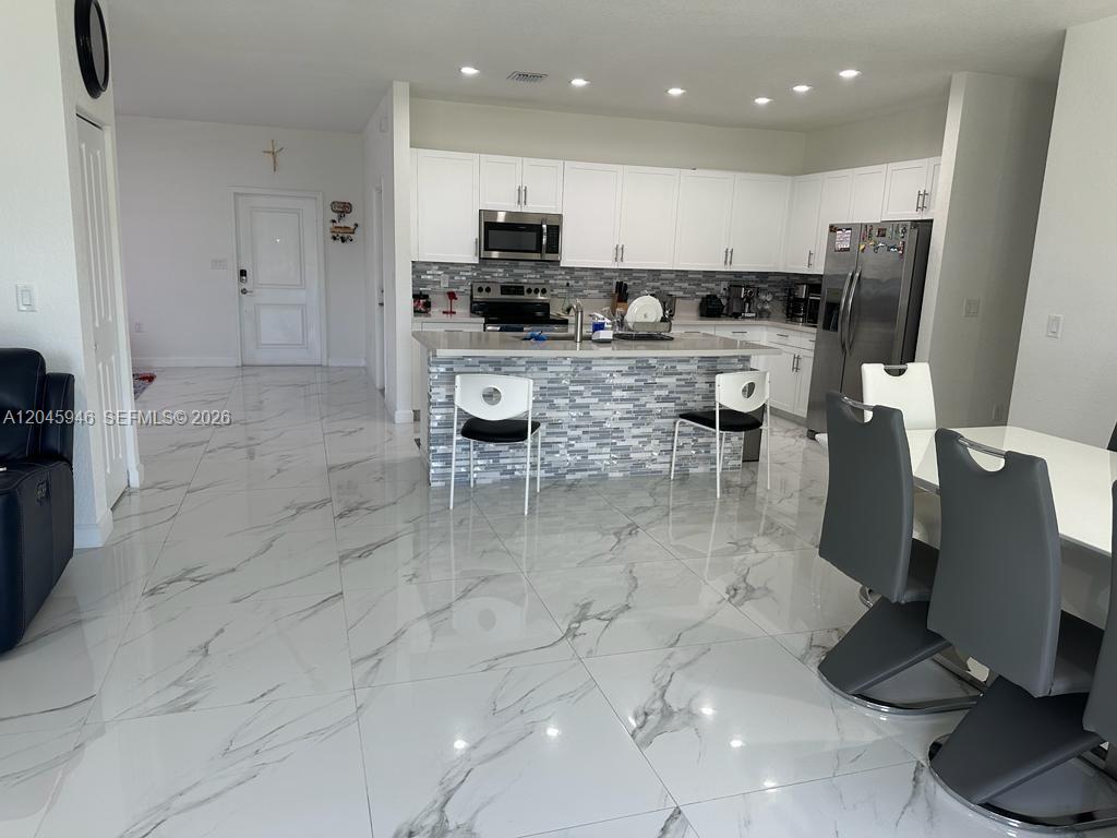 A modern kitchen features white cabinets, a tiled island, and white marble-patterned tile flooring — 12760 SW 215th Ter, Miami FL 33177, MIAMI, FL