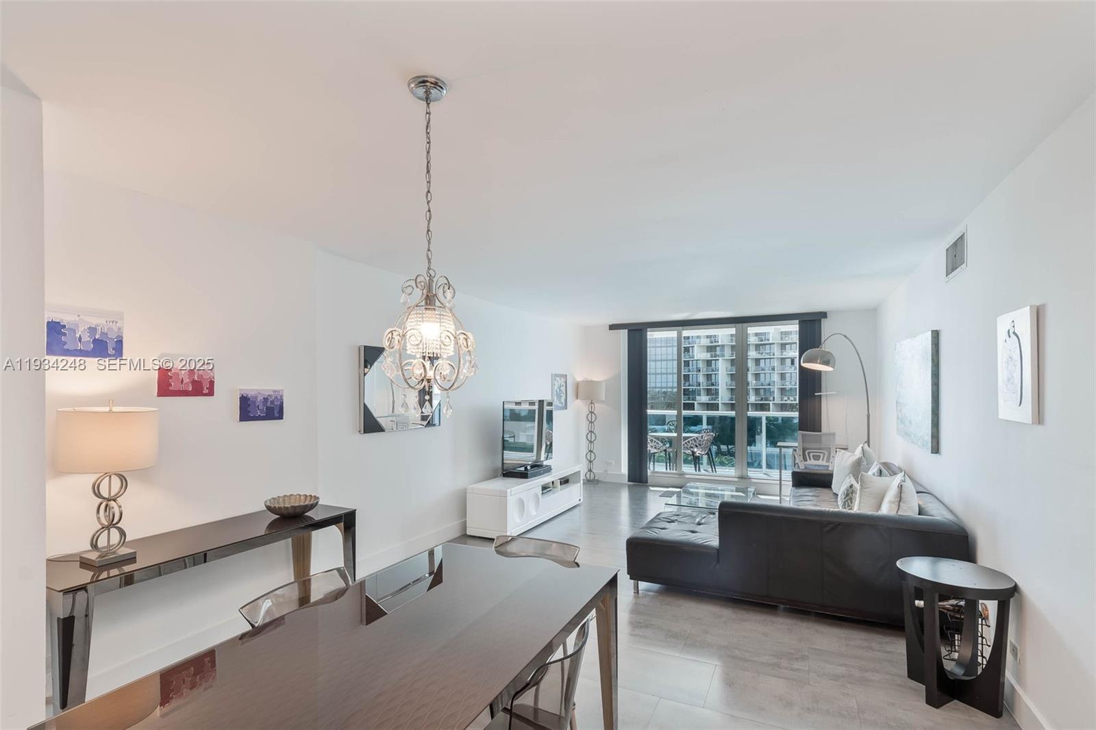 A modern living and dining area features a dark sectional sofa, chandelier, and balcony access — 2301 Collins Ave # 507, Miami Beach FL 33139, MIAMI BEACH, FL