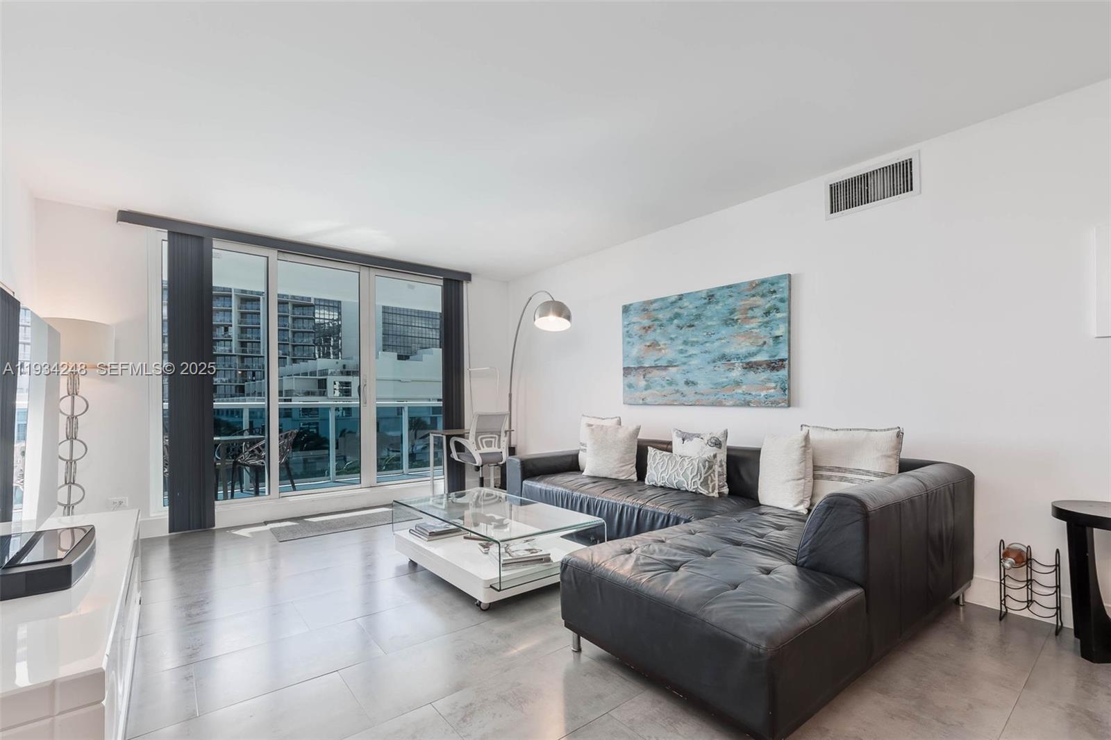 A living room features a black leather sectional, glass coffee table, and floor-to-ceiling windows — 2301 Collins Ave # 507, Miami Beach FL 33139, MIAMI BEACH, FL