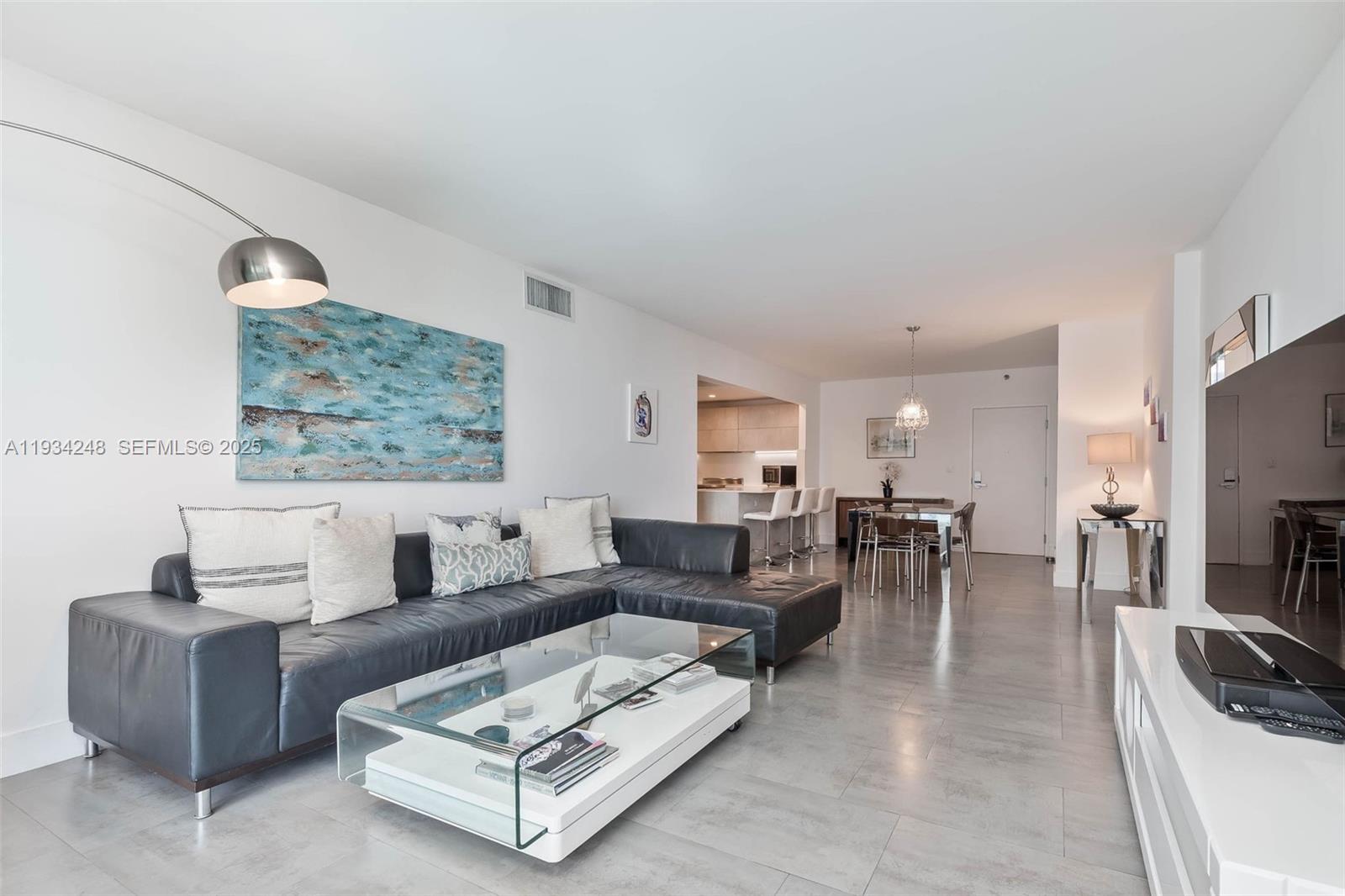 A modern living room features a dark leather sectional, glass coffee table, and tile flooring — 2301 Collins Ave # 507, Miami Beach FL 33139, MIAMI BEACH, FL
