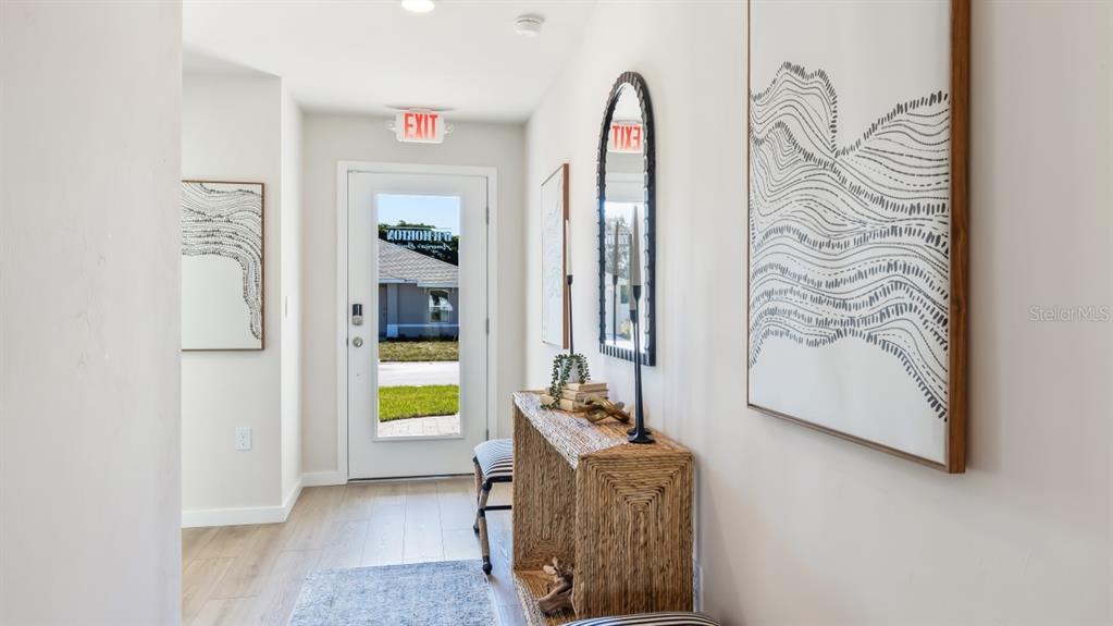 A bright entryway features light wood flooring, a woven console table, and abstract wall art — 1494 POWELL VALLEY DRIVE, PORT CHARLOTTE, FL