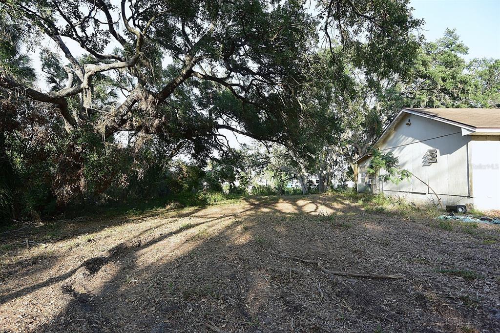 A large, shaded dirt lot sits next to the side of a single-story house — 7610 ANNA AVENUE, GIBSONTON, FL