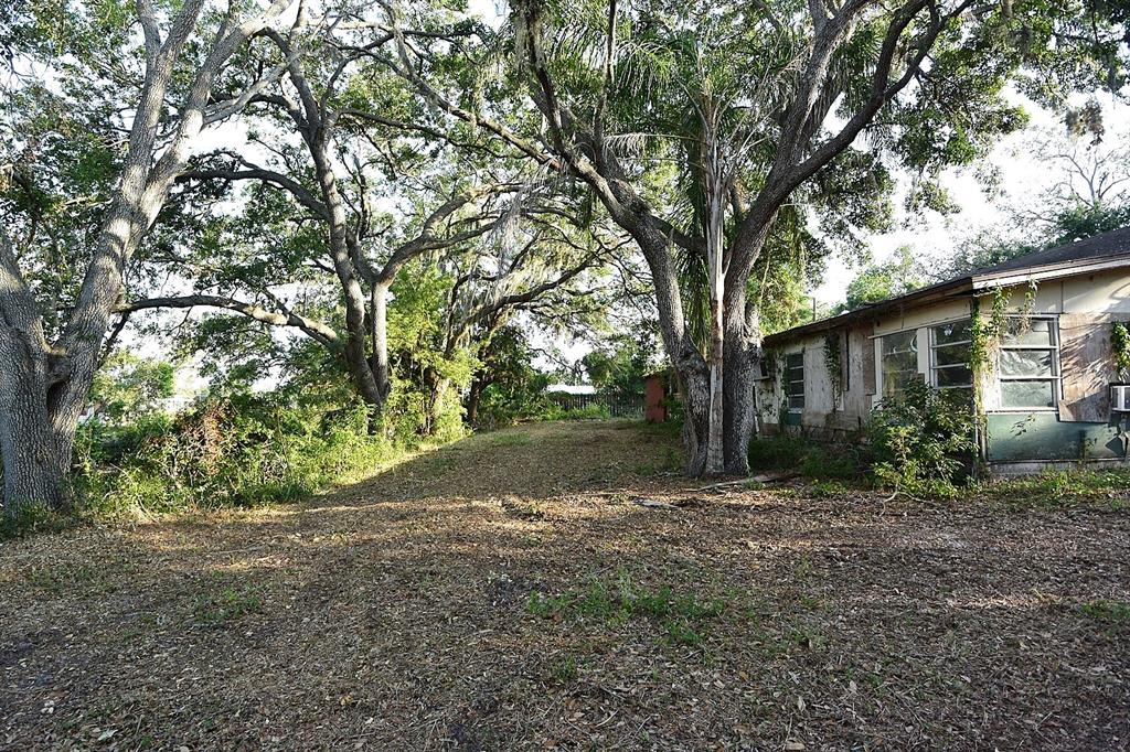 A side view of a weathered house exterior surrounded by large trees and cleared land — 7610 ANNA AVENUE, GIBSONTON, FL