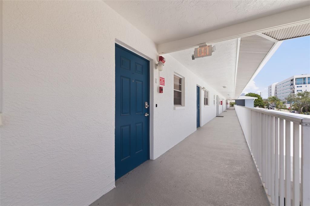 An exterior walkway leads past blue apartment doors along a white building with railings — 3717 46TH AVENUE S UNIT 11, ST PETERSBURG, FL