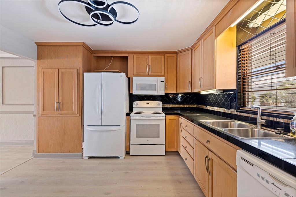 A kitchen features light wood cabinets, black countertops, white appliances, and a modern circular light fixture — 3717 46TH AVENUE S UNIT 11, ST PETERSBURG, FL