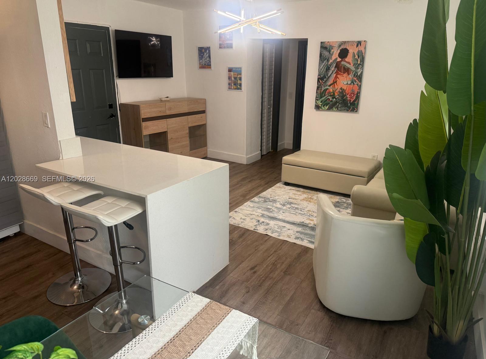 A living room with a kitchen island, white bar stools, and a large potted plant — 7928 Harding Ave # 2, Miami Beach FL 33141, MIAMI BEACH, FL