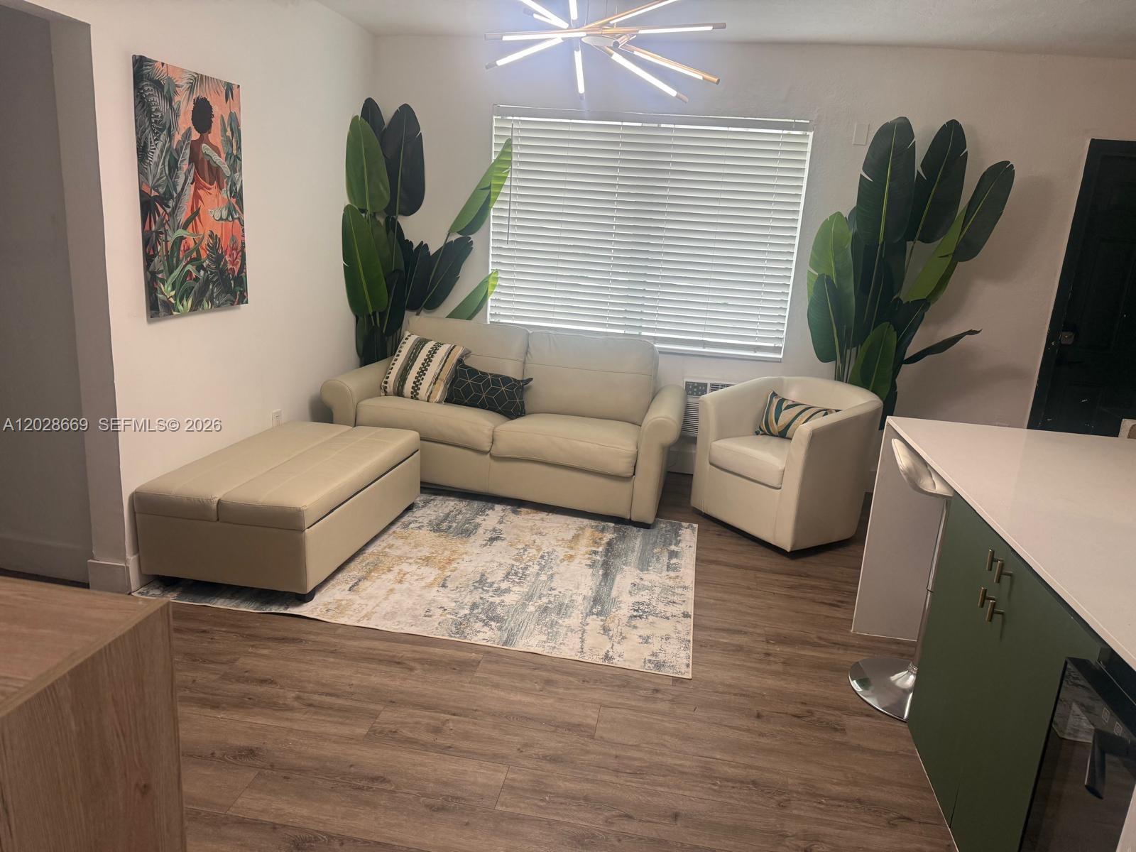 A living room features a beige sofa, matching ottoman, armchair, and large potted plants — 7928 Harding Ave # 2, Miami Beach FL 33141, MIAMI BEACH, FL