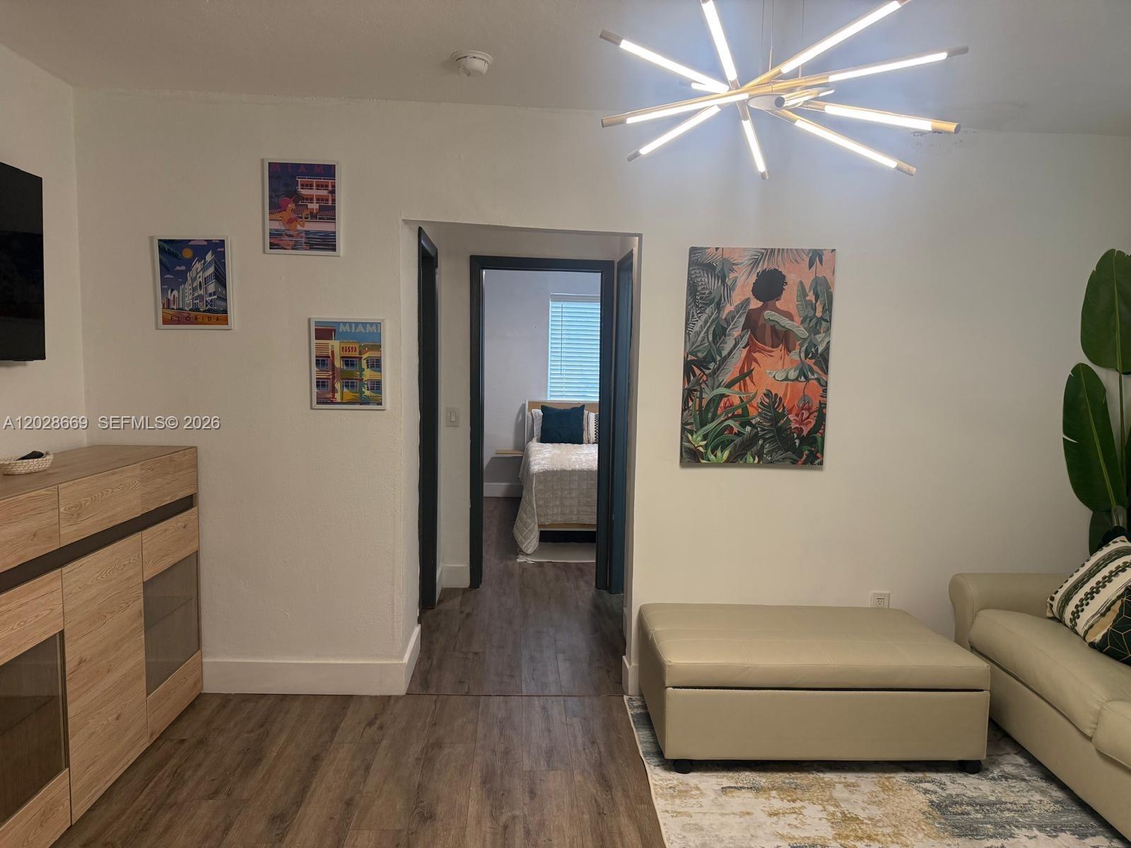 A living room with wood-look flooring, a modern chandelier, and a doorway leading to a bedroom — 7928 Harding Ave # 2, Miami Beach FL 33141, MIAMI BEACH, FL