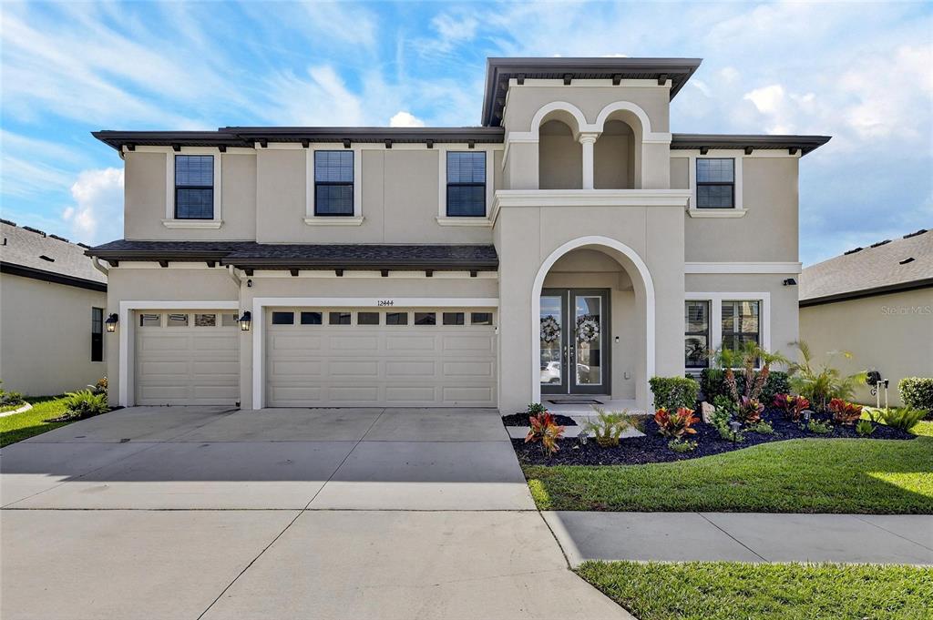 A two-story suburban house with a three-car garage and an arched entryway at dusk — 12444 HORSESHOE BEND DRIVE, LITHIA, FL