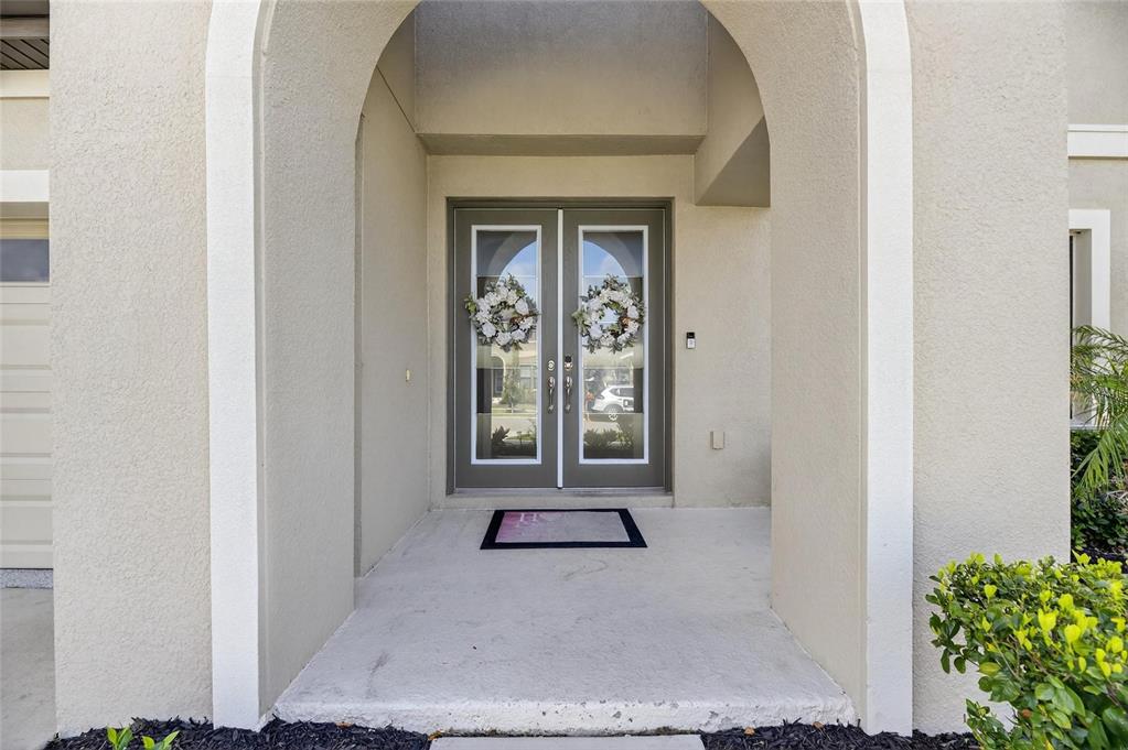 A covered entryway features a double glass door with wreaths and a concrete porch — 12444 HORSESHOE BEND DRIVE, LITHIA, FL