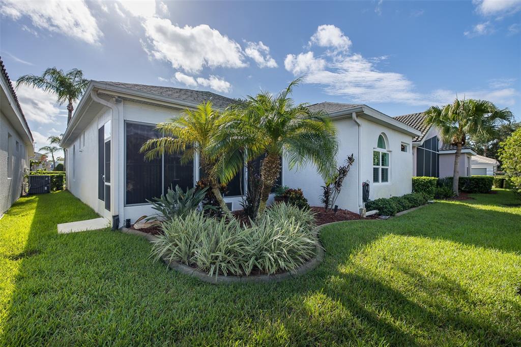 The exterior of a white house features a screened-in lanai and a landscaped garden bed — 1239 STADLER DRIVE, NEW PORT RICHEY, FL